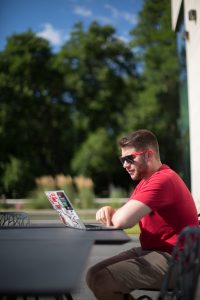 Man wearing sunglasses types on a computer outdoors